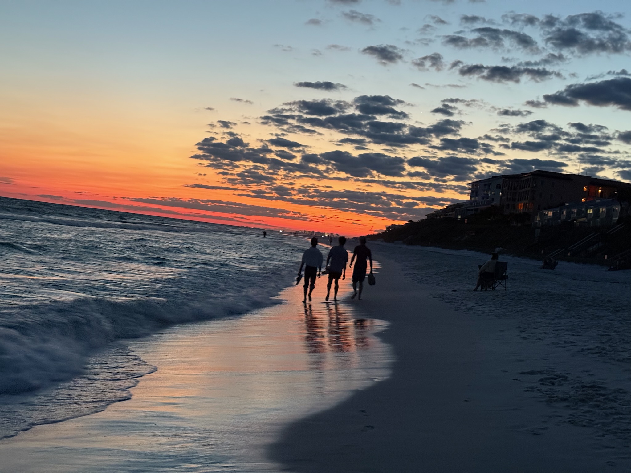 Photo of three sillouettes walking down the sea line at sunset.